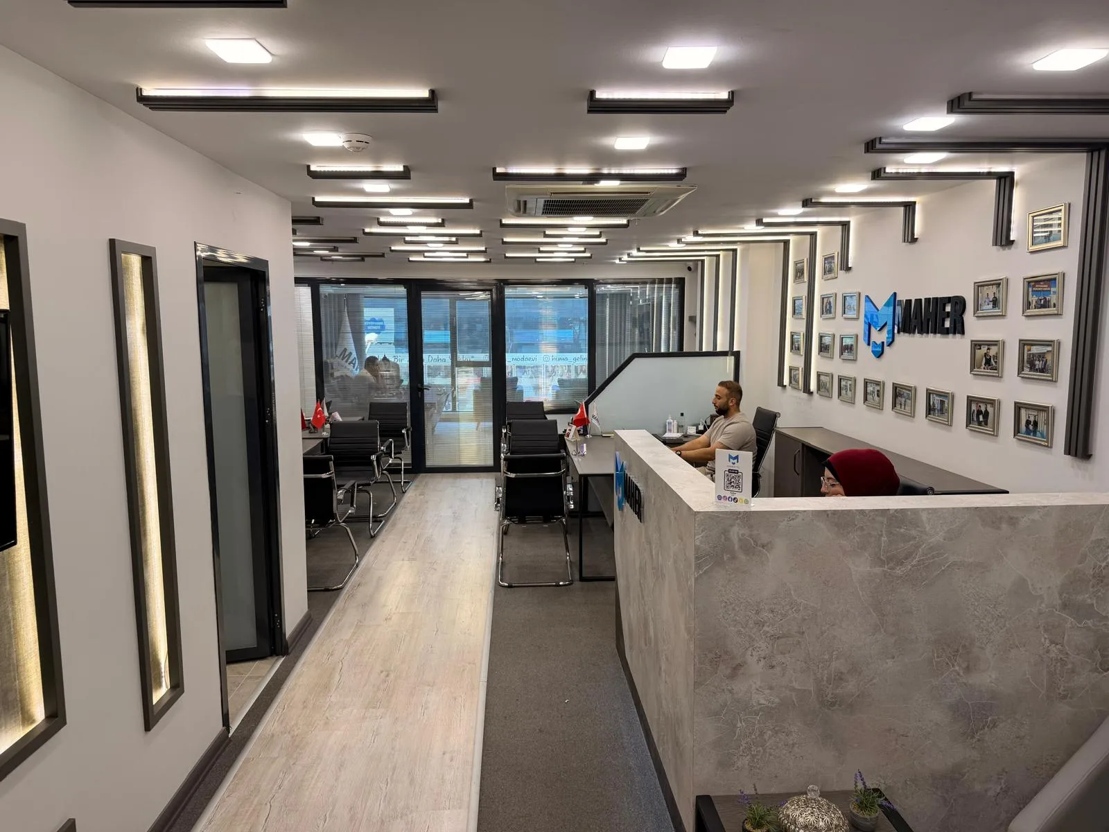 Reception desk backed by a wall of framed photographs and the Maher logo